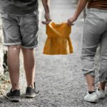 A couple standing outdoors holding a yellow baby dress symbolizing a future addition to their family.